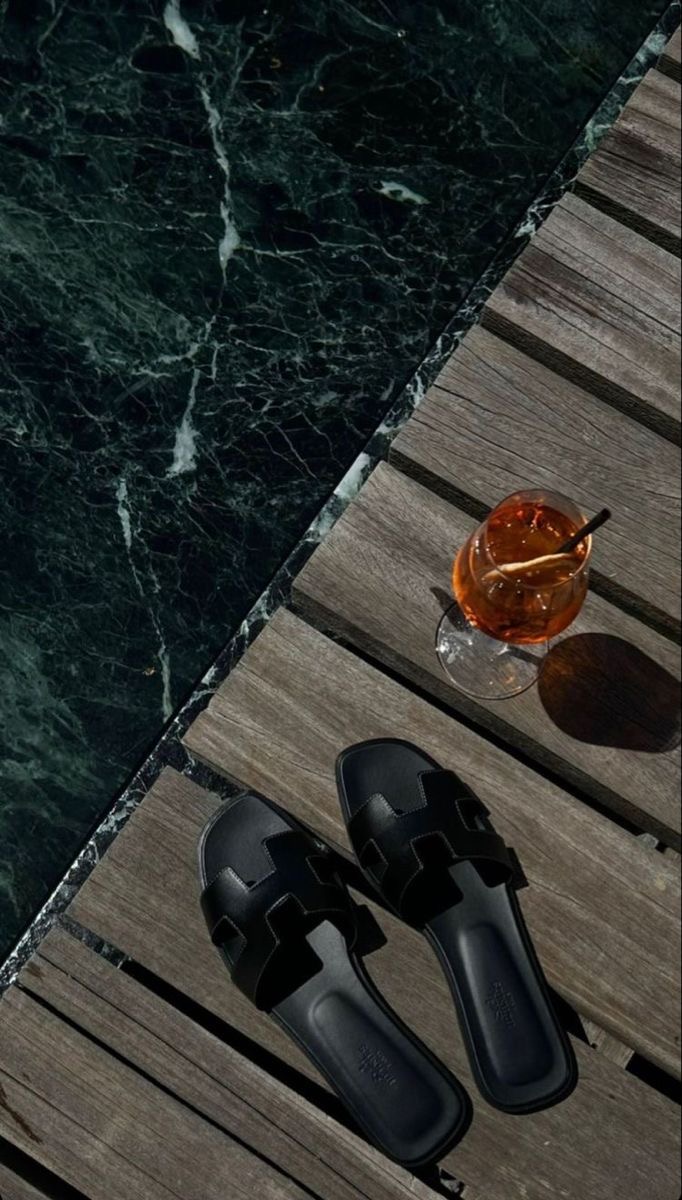 Svarta Hermès Oran-sandaler vid poolkant i marmor